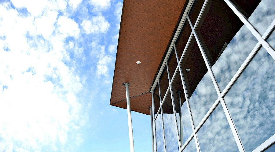 A shot from below of glass windows on a building beneath a cloudy blue sky.
