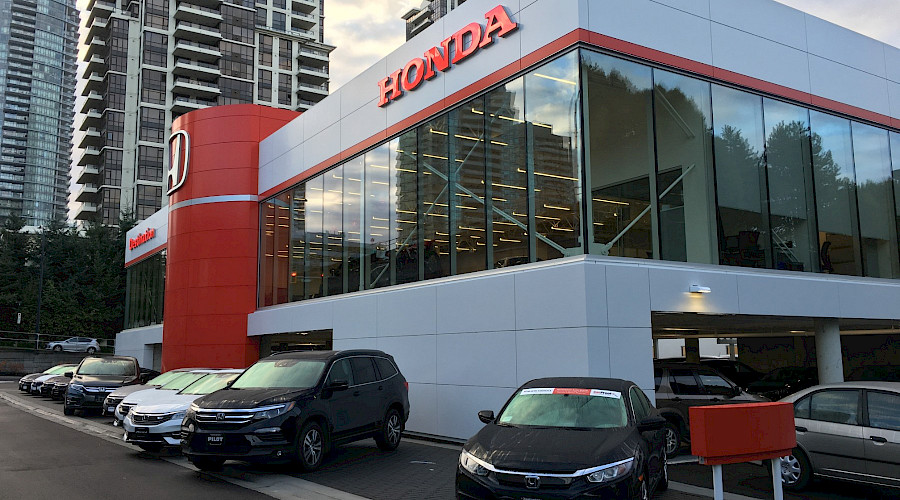 Rows of cars in front of the red and white exterior of Destination Honda.