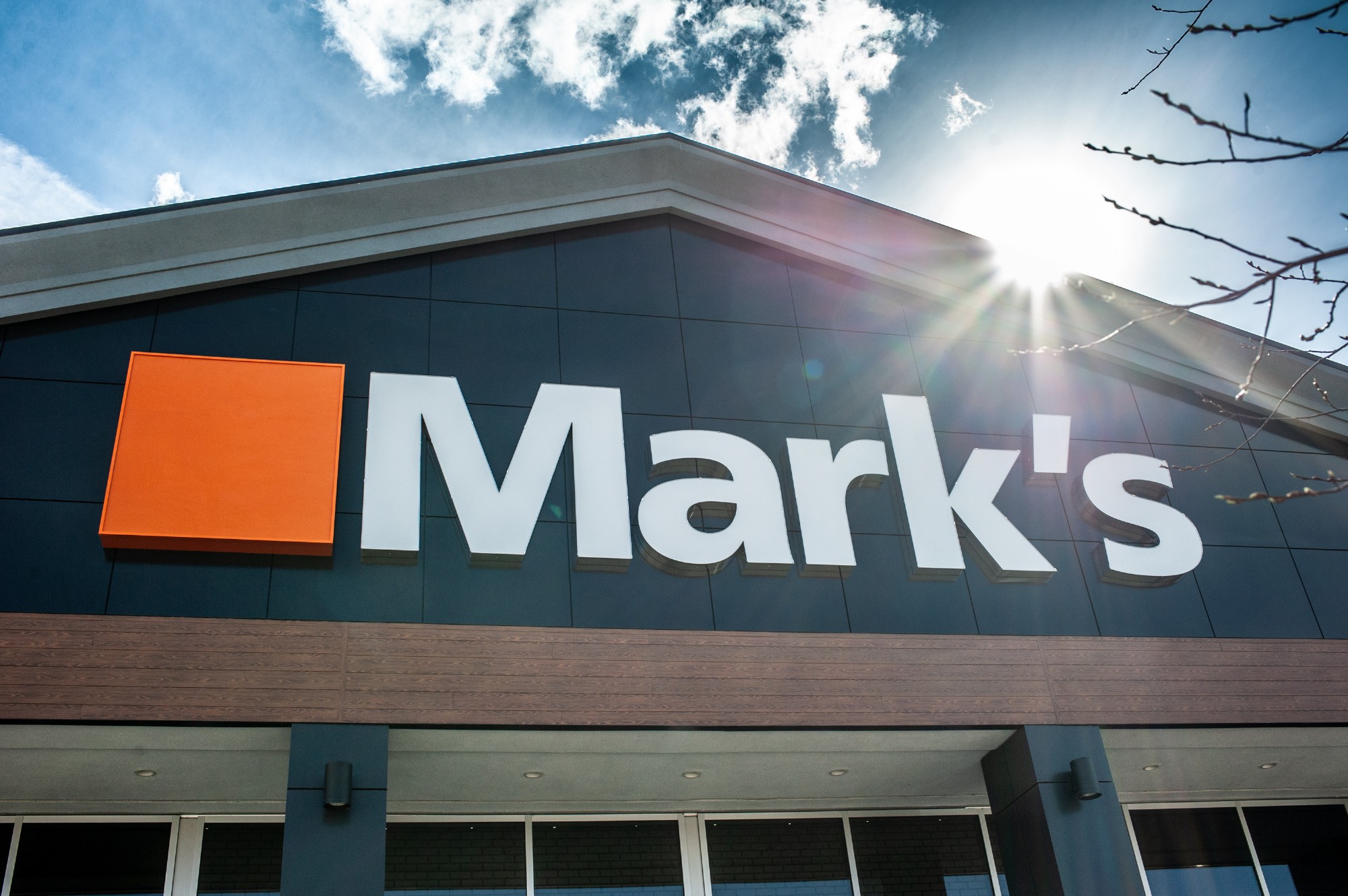 Exterior image of the Mark's Work Wearhouse entrance which feature's the company logo and a bright blue sky, built by Chandos Construction Red Deer.