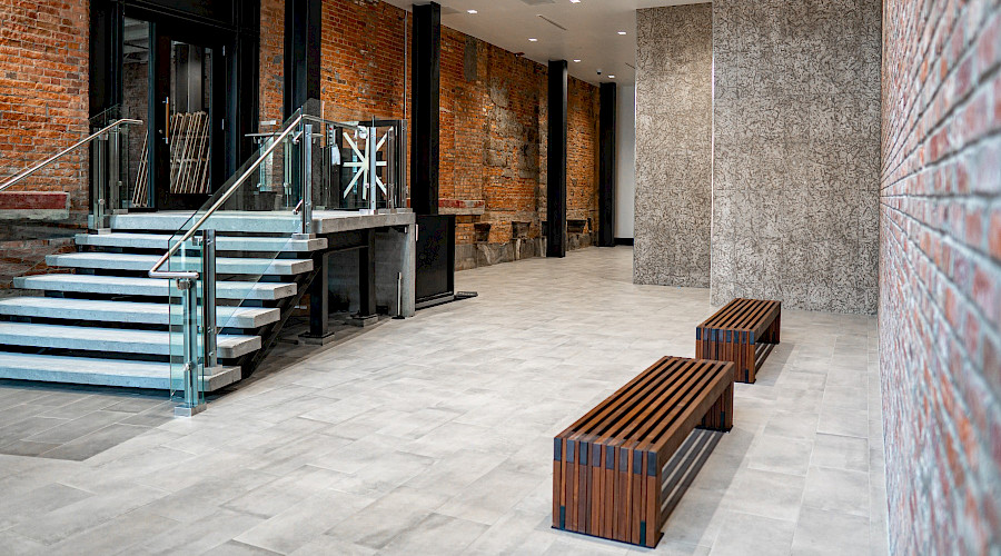 Two wooden benches and a staircase in an open room with brick walls.