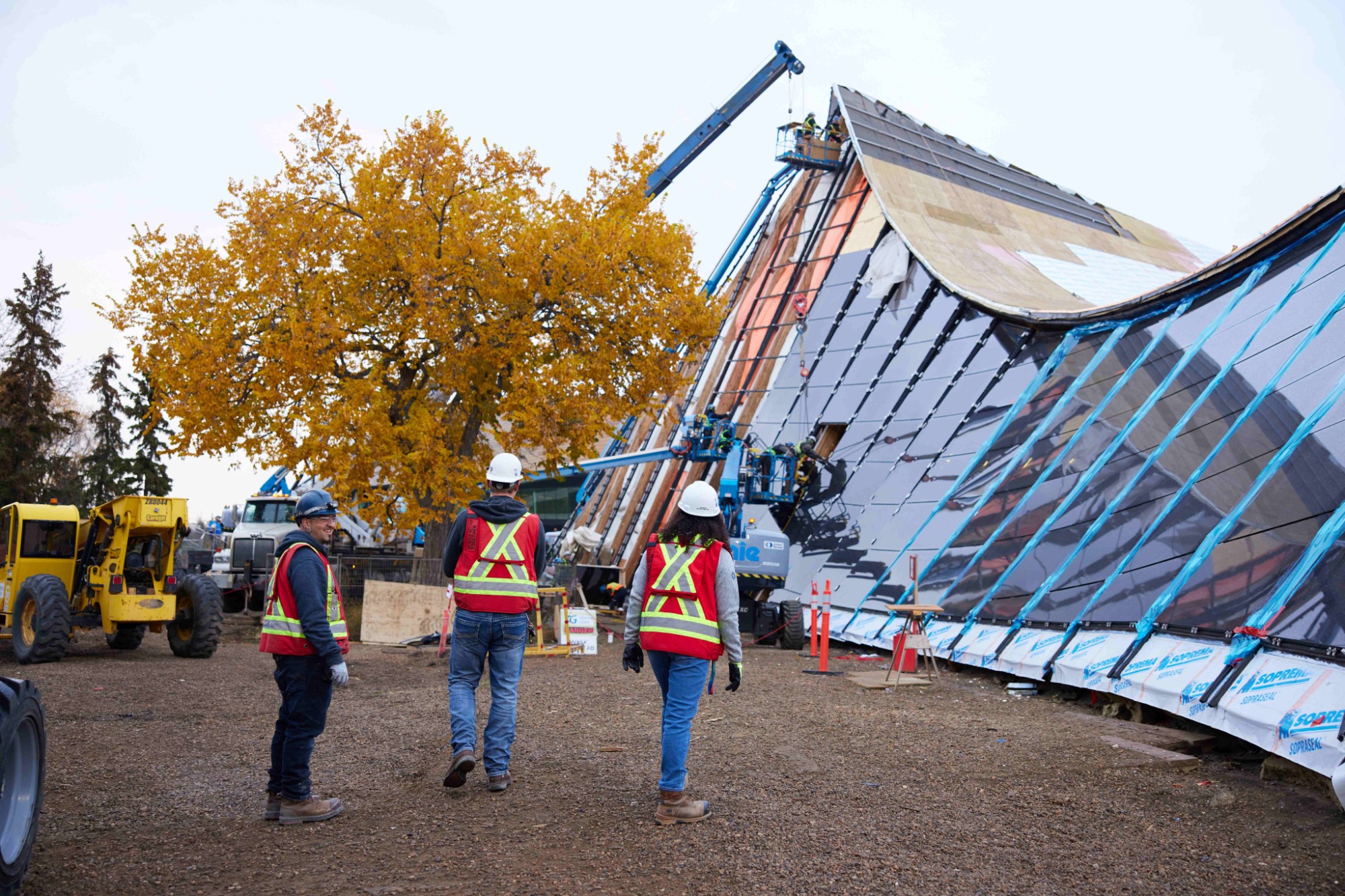 Image of three Chandos Construction Edmonton workers completing a site walk through to check for safety at the Peter Hemingway Leisure Centre. Crane installing new copper roof in background