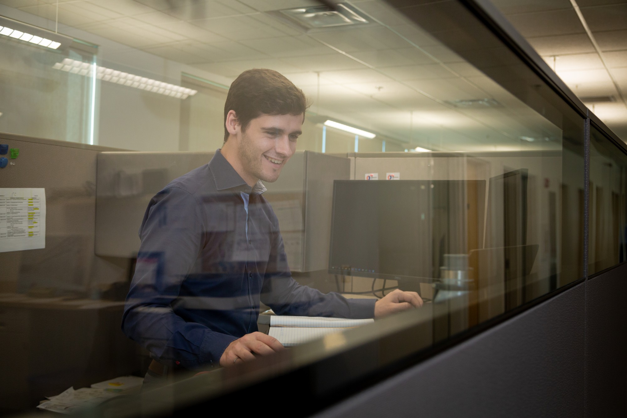 A Chandos office worker smiling at his desk while working on his computer.