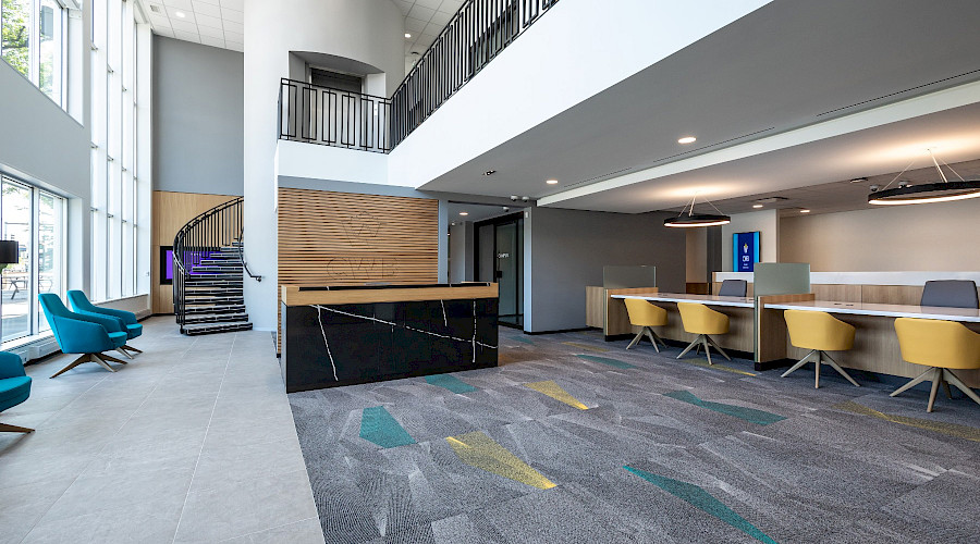 Interior shot of the newly completed lobby at the Canadian Western Bank in Lethbridge, built by Chandos Construction Calgary. The image features a circular staircase that leads to the upper floor, brightly coloured teal seats, and yellow chairs at the teller's desk.