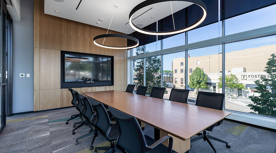 Interior shot of the board room at the Canadian Western Bank in Lethbridge, Alberta, built by Chandos Construction Calgary. The accent wall features a large TV with decorative wood paneling, grey walls, and large windows.